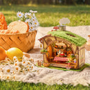 The Robotime Fluffy Grove, along with flowers and a bread basket, on a picnic blanket