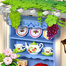 Pergola with grapevines and underneath it a blue cabinet displaying tableware in the Robotime Midsummer Dream Yard