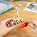 A person is assembling one of the sailboats from the Robotime Red Boats set