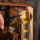 A person using tweezers to put a book on a shelf in the Robotime Sam’s Study